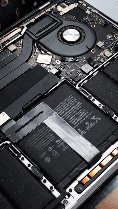 A laptop opened up showing the motherboard, cooling fan and battery